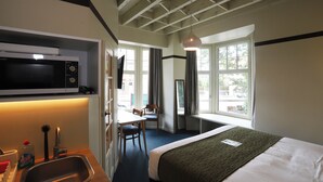 Une chambre d’hôtel équipée d’un lit, d’un bureau, d’une chaise, d’un four à micro-ondes, d’un lavabo et de grandes fenêtres.