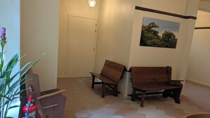 Une pièce avec un banc en bois, une porte, un tableau accroché au mur et une plante en pot.