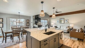 A modern kitchen with a marble island, wooden dining table, and ceiling fans.