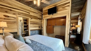 A bedroom with a bed, a nightstand, a lamp, a wooden headboard, and a television mounted on the wall.