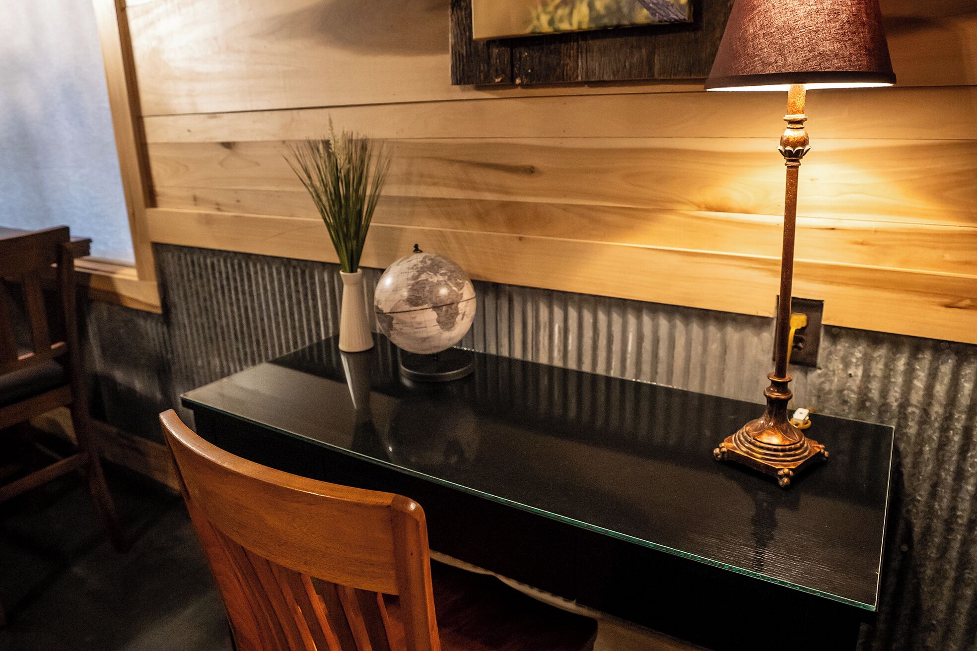 A wooden wall with a globe and a vase of green plants on a black table.