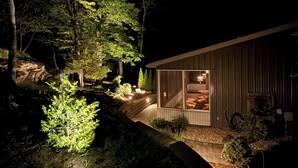 A modern house with a large glass window, surrounded by trees and a stone pathway.