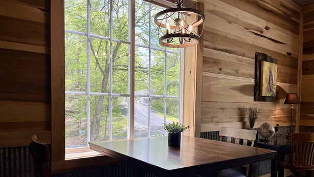 A wooden interior with a large window, a dining table, chairs, and a hanging light fixture.