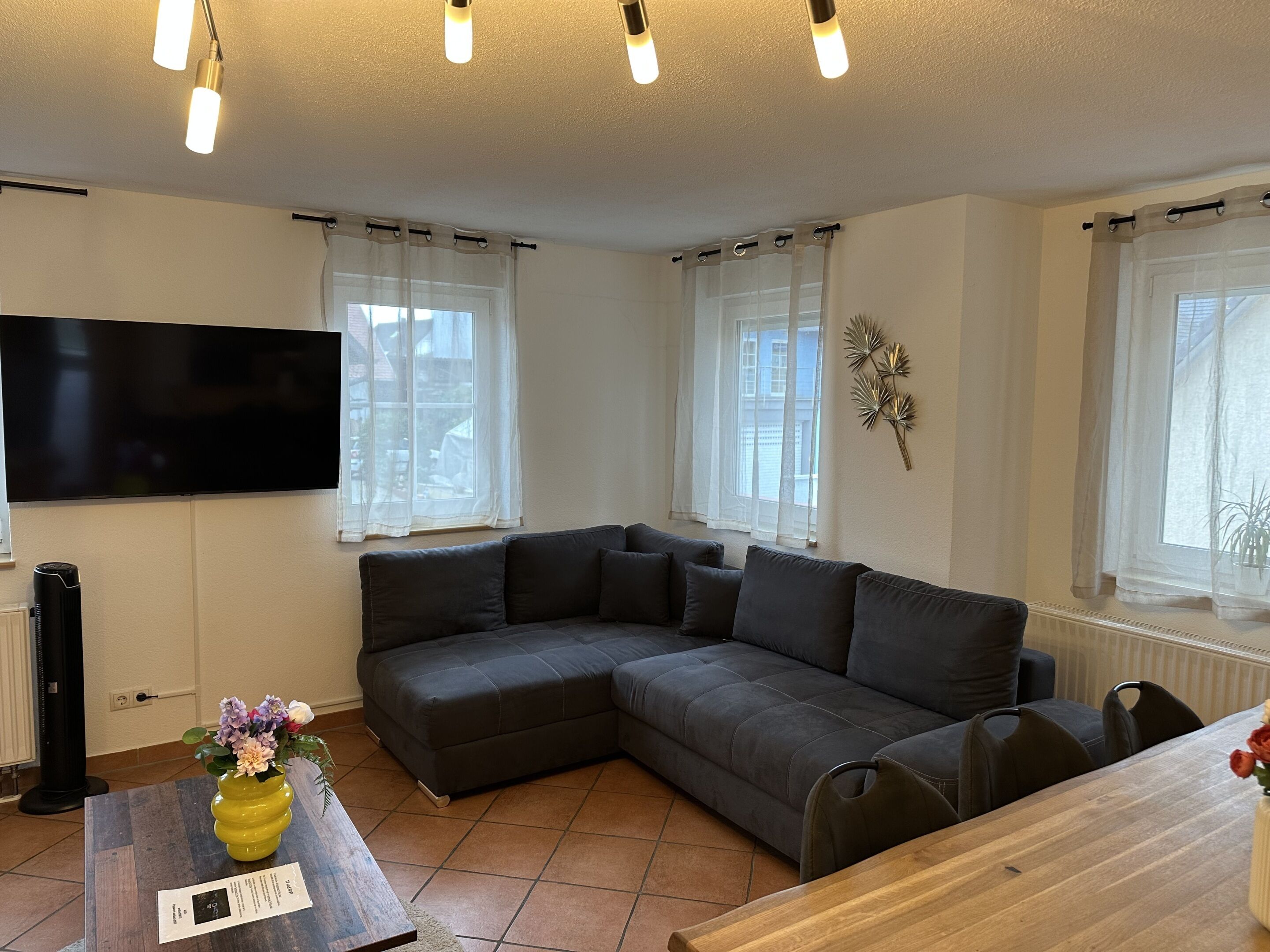 A modern living room with a sectional sofa, a flat-screen TV, and a wooden dining table.