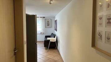 Un couloir avec une porte, un canapé, une chaise et un tableau encadré au mur.