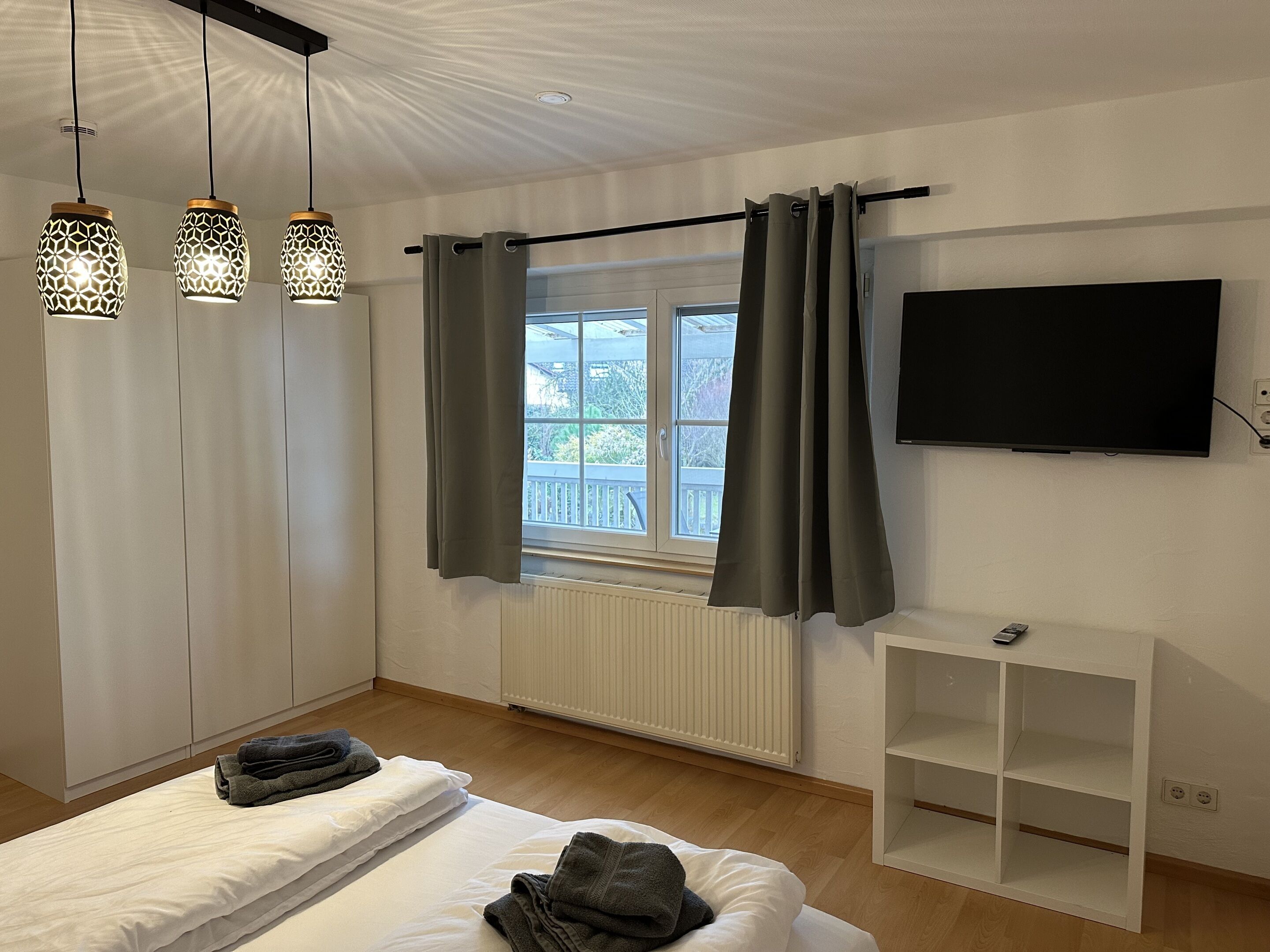 A bedroom with a bed, a TV, a window with curtains, and a radiator.
