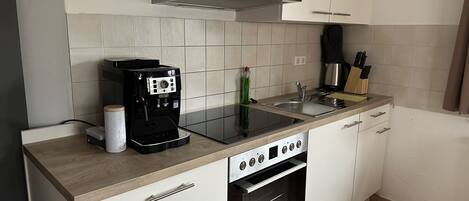 A compact kitchen with a coffee maker, a kettle, a sink, and a stove.