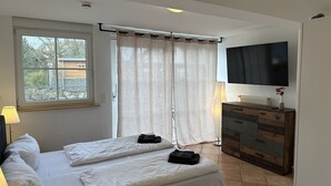 A bedroom with a bed, a TV, a dresser, and a window with curtains.