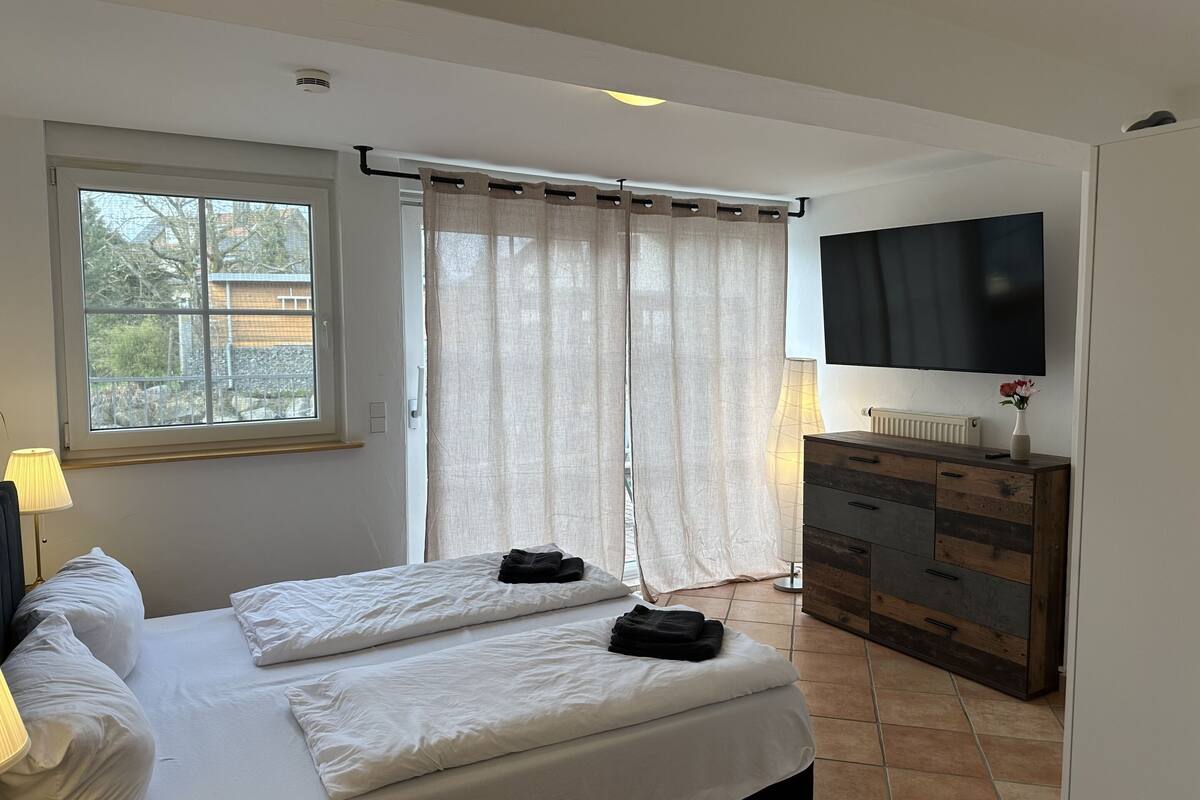 Une chambre à coucher avec un lit, une télévision, une commode et une fenêtre avec des rideaux.
