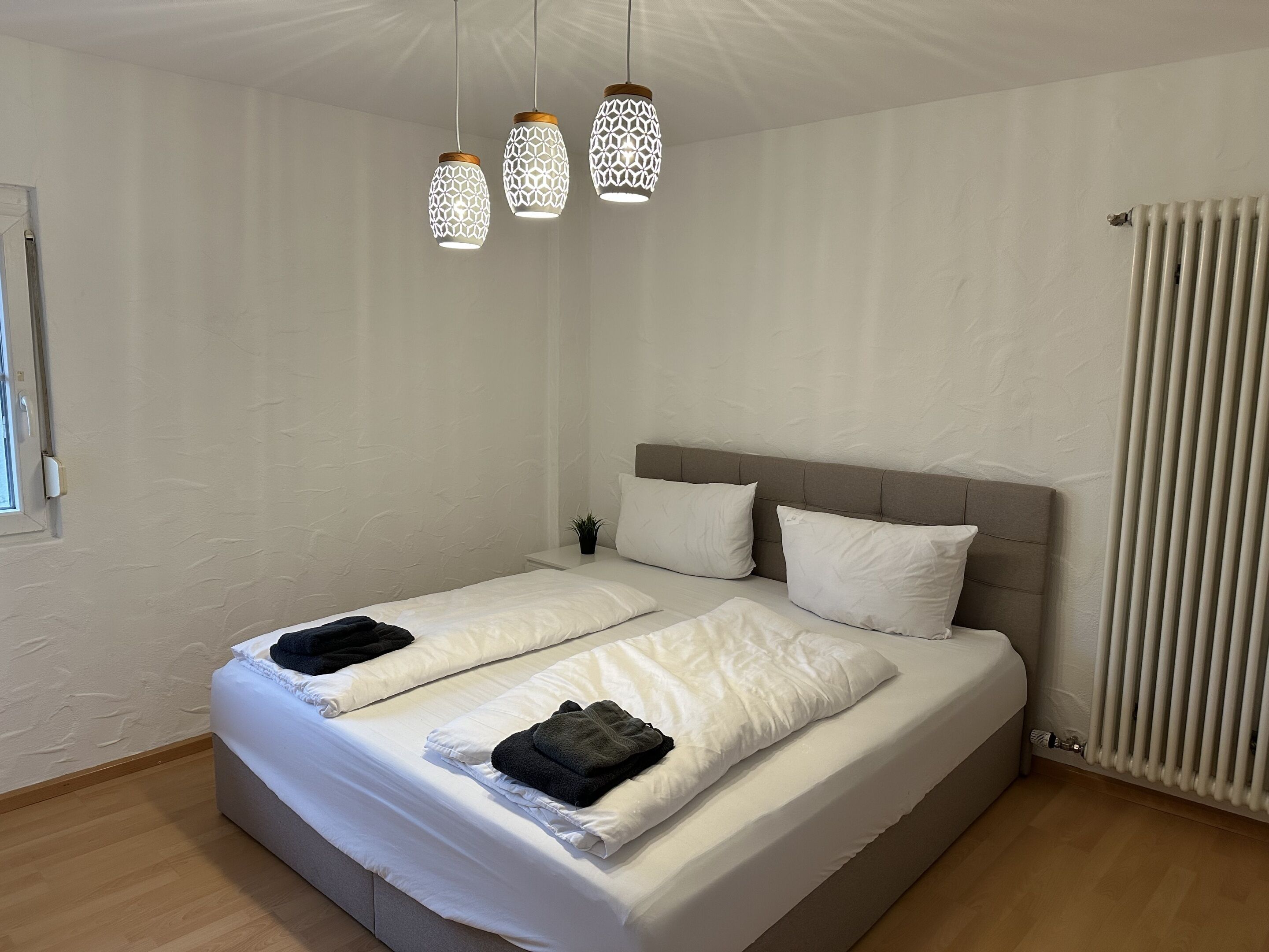 A double bed with white bedding, a grey headboard, and three hanging pendant lights.