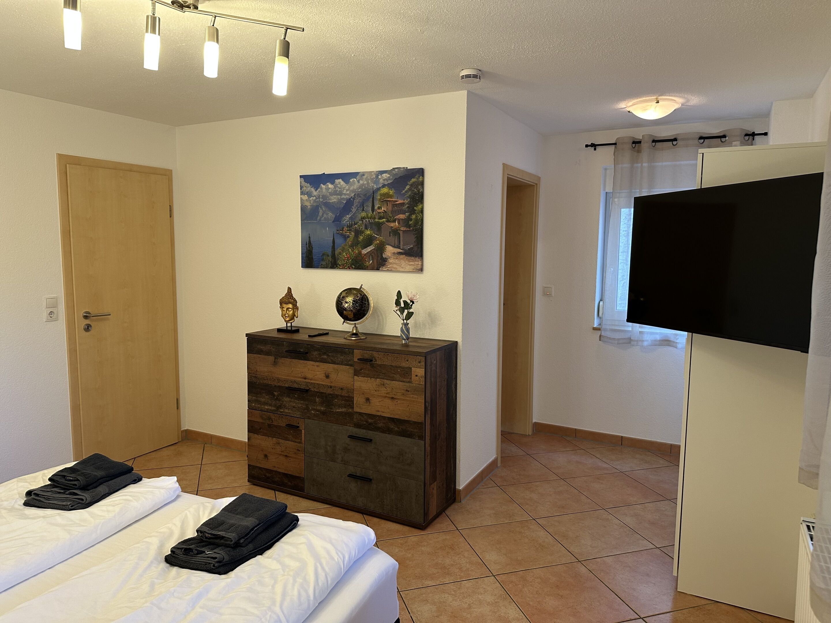 Un dormitorio con una cama, un aparador, un cuadro y un televisor.