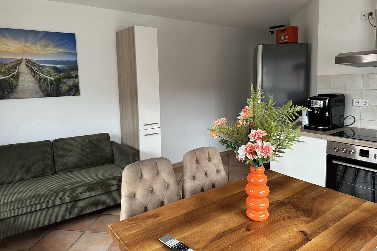 Une cuisine moderne avec une table à manger en bois, un canapé et un tableau représentant un paysage.