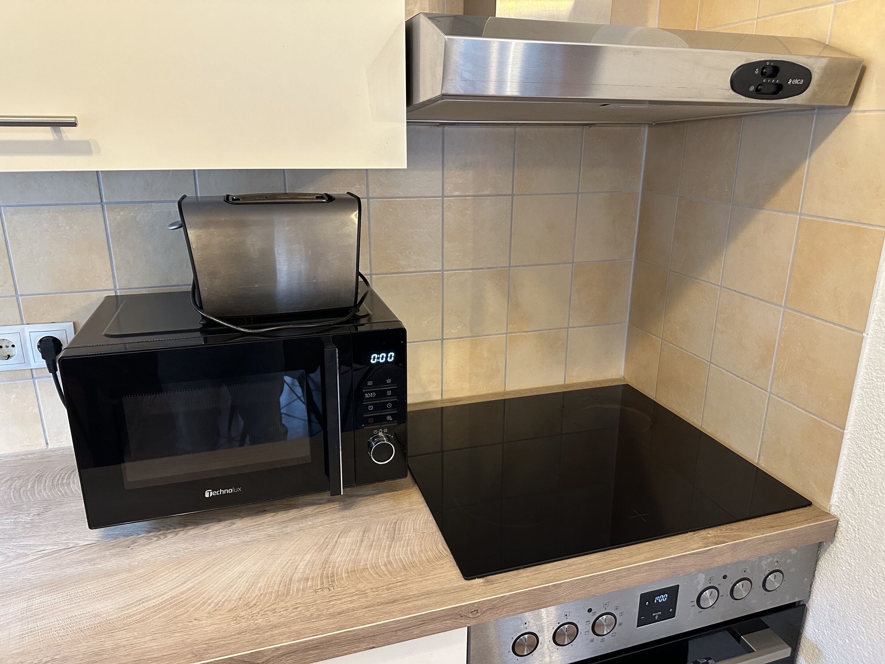 Una cocina con un microondas negro, un horno empotrado y una campana extractora de acero inoxidable.
