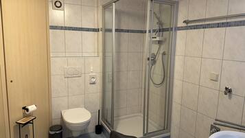 A bathroom with a glass-enclosed shower, a toilet, a sink, and a towel rack.