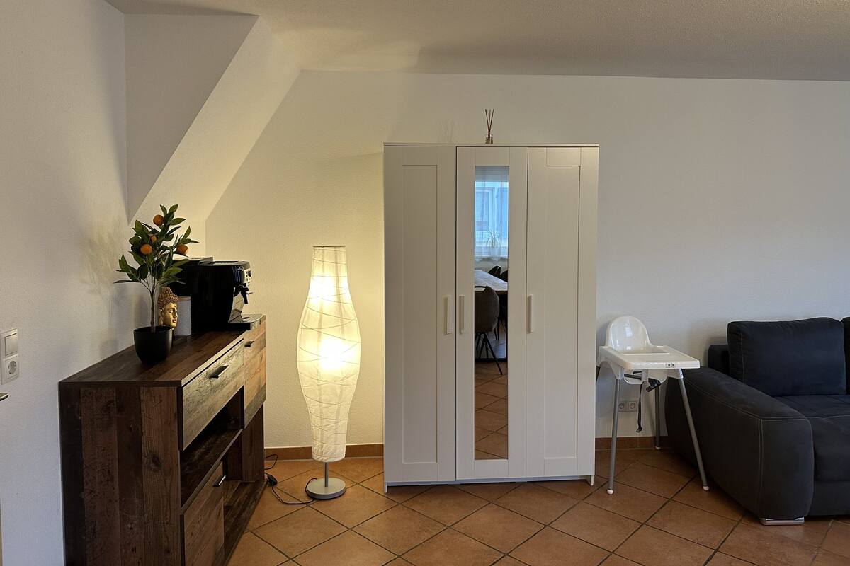 Un salon comprenant un canapé, une table basse, une lampe, un meuble orné d’une statue de Bouddha et une armoire avec un miroir.