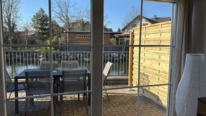 A patio with a table and chairs, a wooden fence, and a view of a pond and houses.