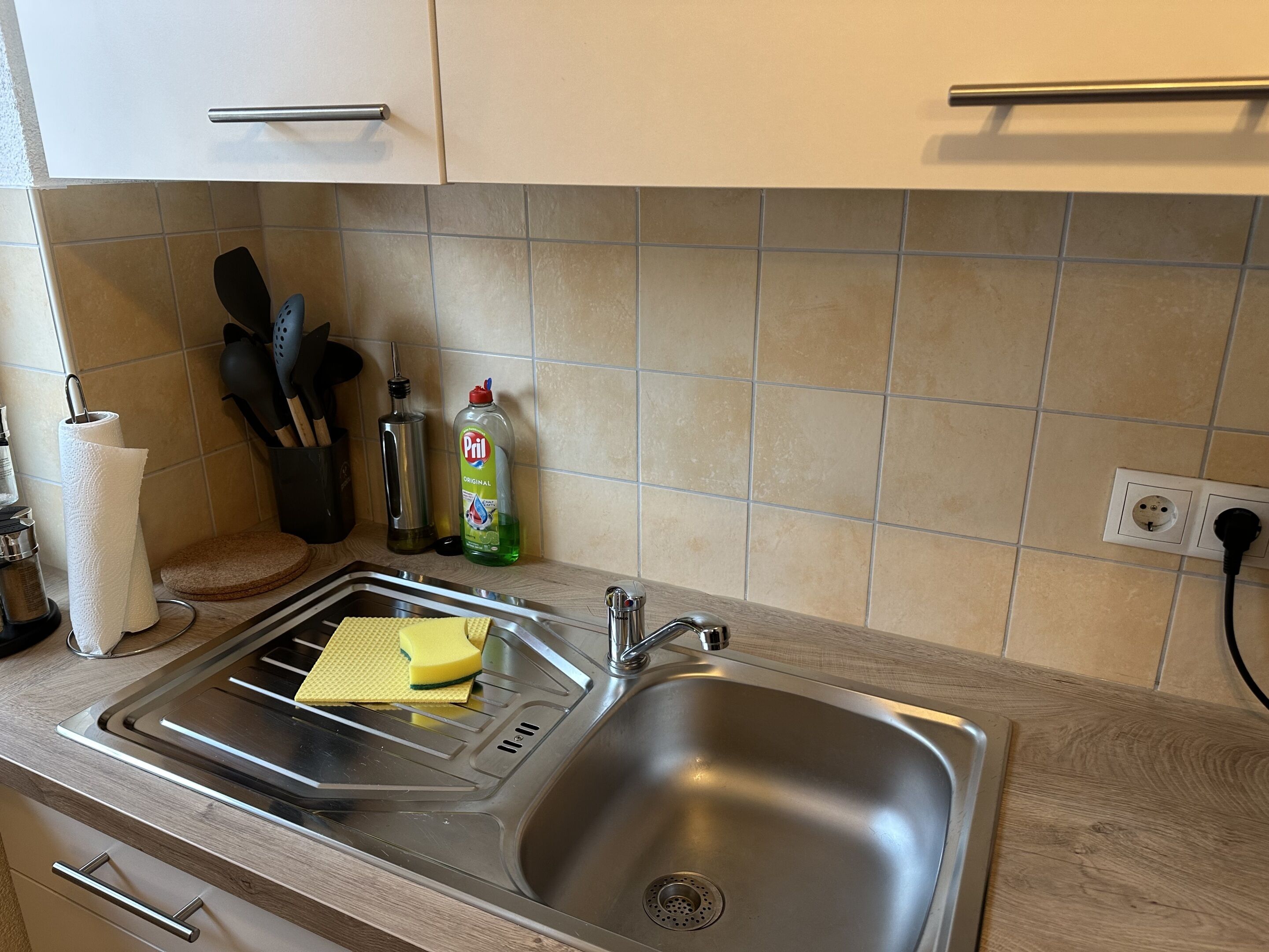 A kitchen with a stainless steel sink, a dish rack, a paper towel holder, a bottle of dish soap, and a knife block.