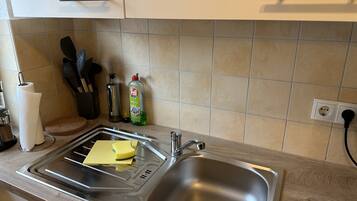 A kitchen with a stainless steel sink, a dish rack, a paper towel holder, a bottle of dish soap, and a knife block.