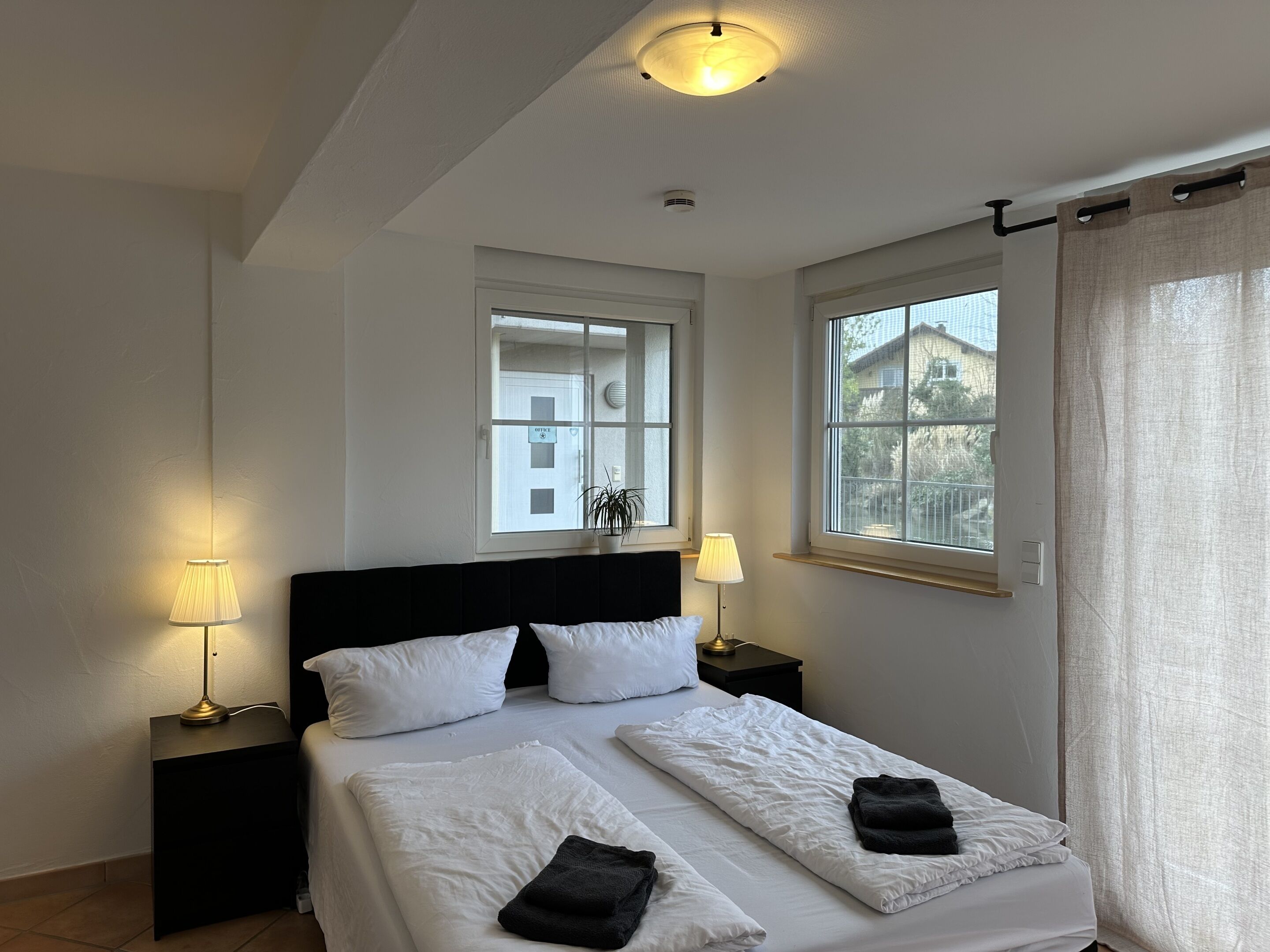 Una camera d'albergo con un letto, due comodini, una finestra e una lampada a soffitto.