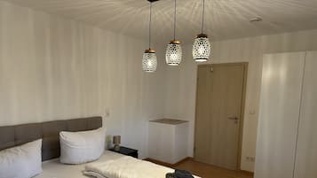 A neatly made bed with white linens, a bedside table with a lamp, and a wardrobe.