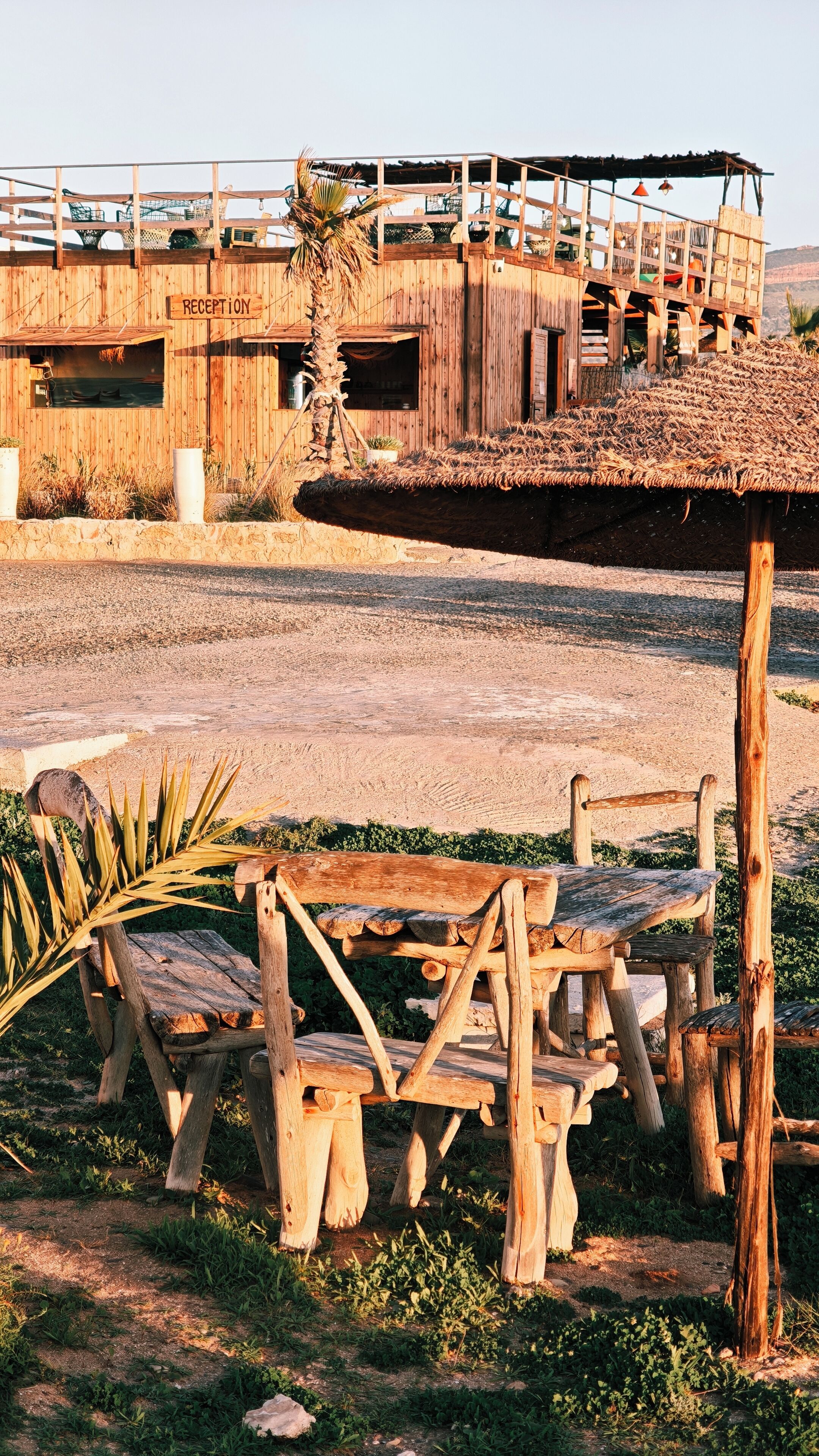 Un bâtiment rustique en bois, doté d’un espace d’accueil, de sièges en plein air et d’une structure à toit de chaume.