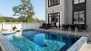 Un área de piscina moderna con piscina azul cristalina, sillas de descanso y un comedor con mobiliario exterior.