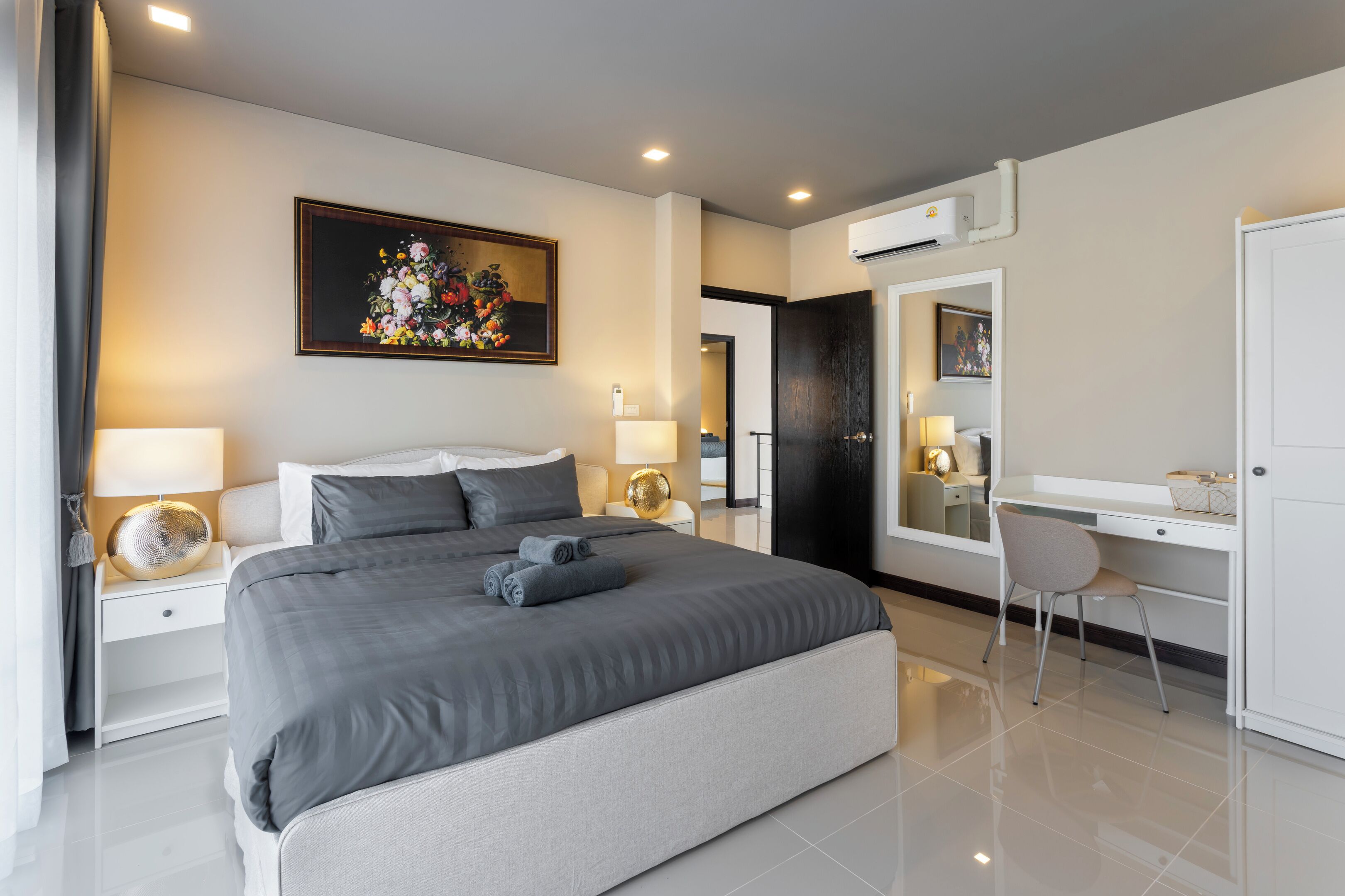 A modern hotel room with a large bed, bedside tables with lamps, a desk with a chair, and a painting on the wall.