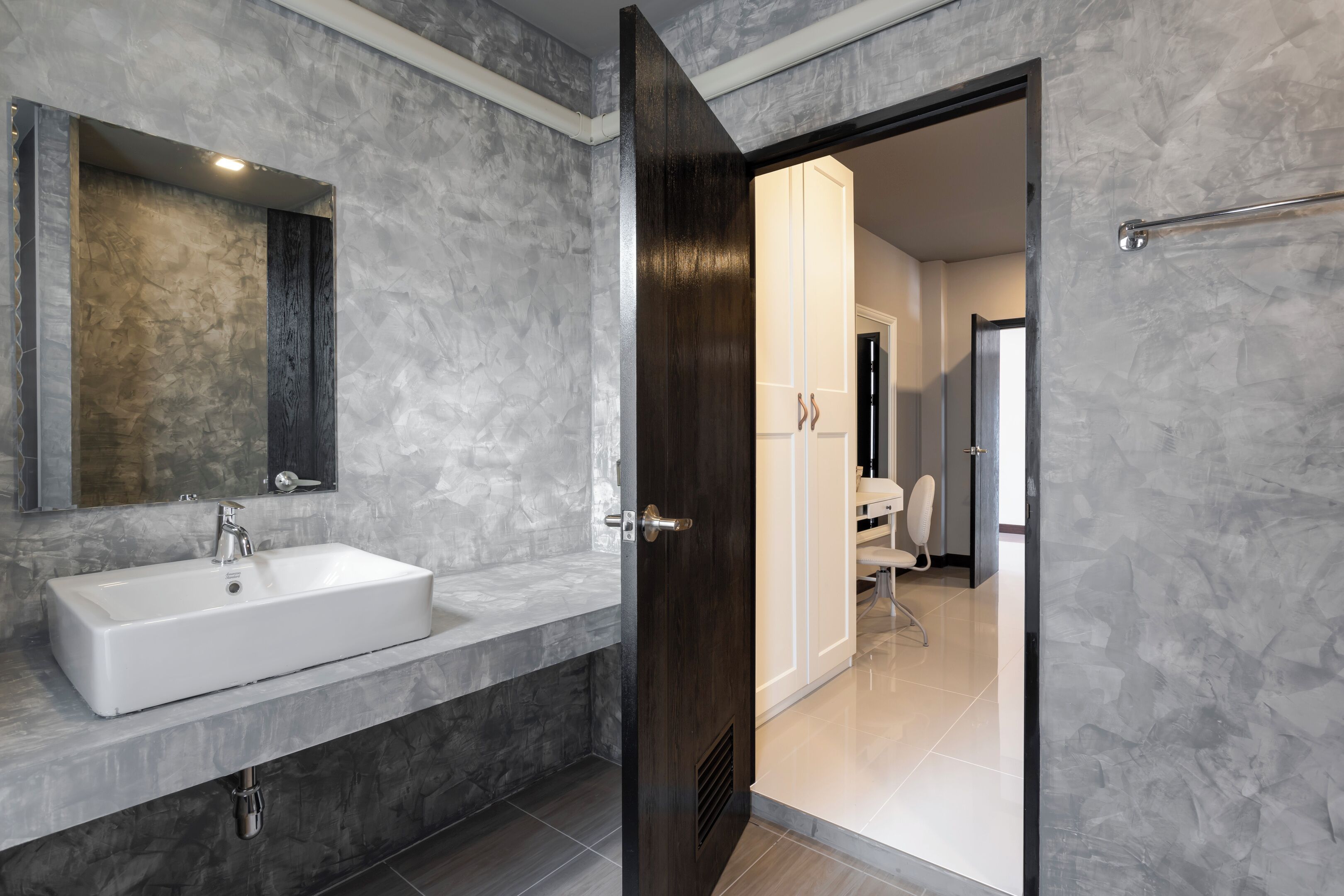 Un baño moderno con lavamanos blanco, puerta de madera oscura y salpicadero de mármol.