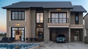 Una casa de dos pisos con piscina, garaje cubierto y balcón.