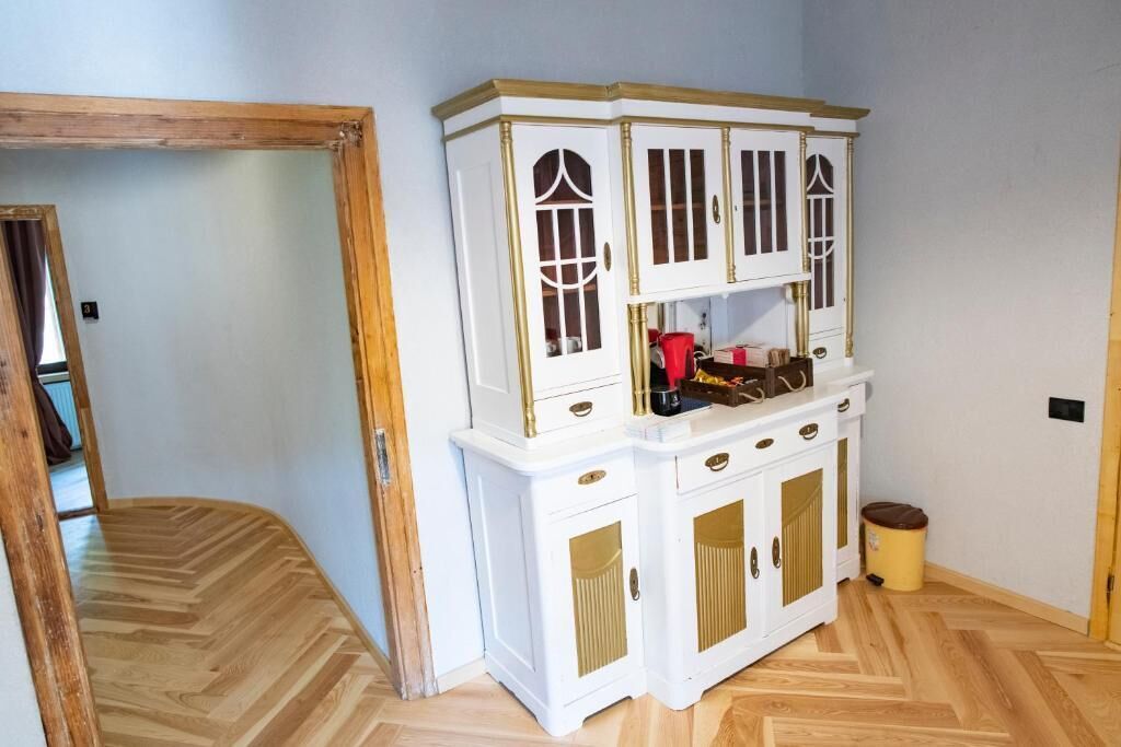 A room with a white cabinet with glass doors and gold handles, a wooden floor, and a door leading to another room.
