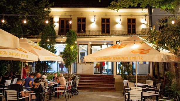 Un espacio de comedor al aire libre con mesas, sillas, sombrillas y luces colgantes.