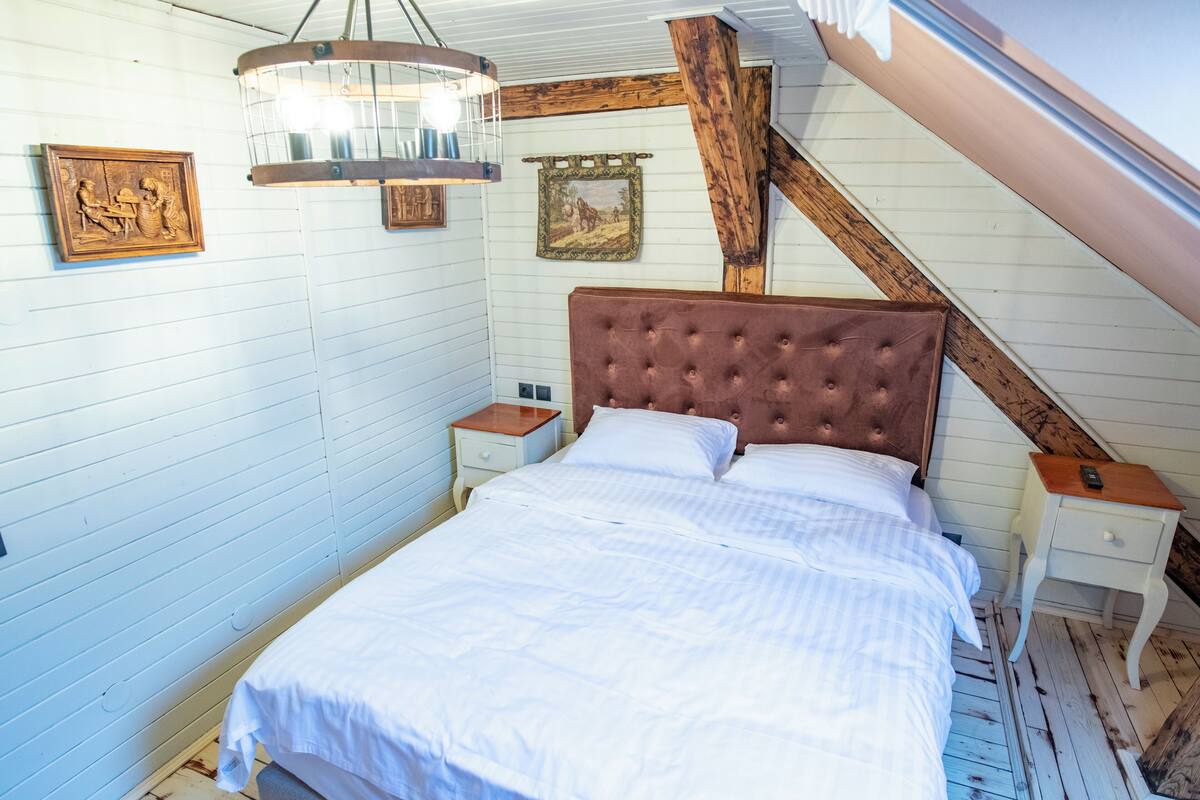 Un dormitorio con una cama grande, vigas de madera, una lámpara colgante y dos mesitas de noche.