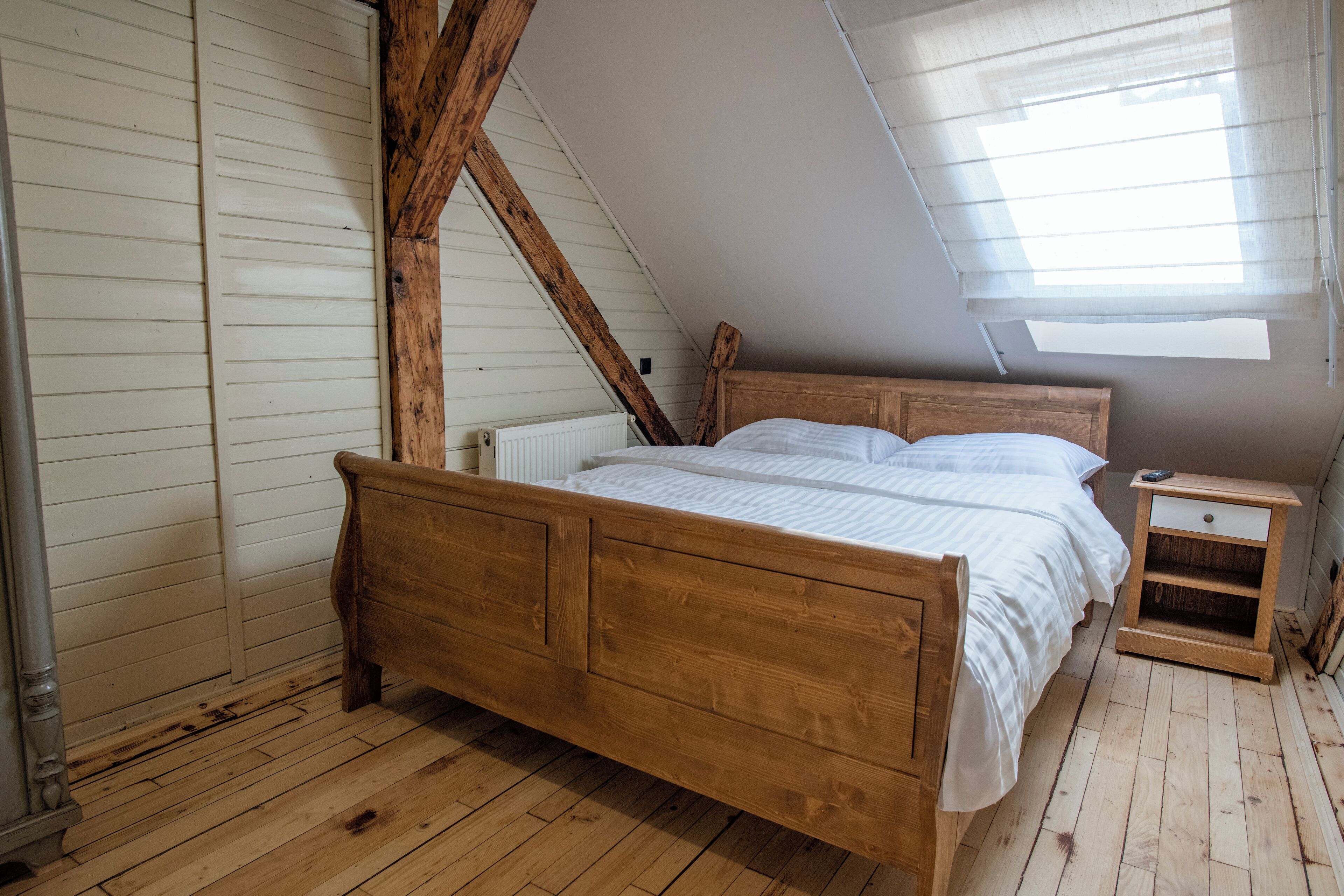 A bedroom with a wooden bed, a nightstand, and a sloped ceiling with skylight.