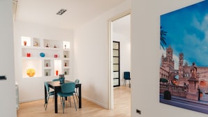 A modern dining area with a wooden floor, a table with chairs, and a wall-mounted shelf with decorative items.