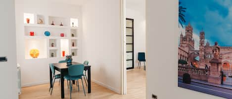 A modern dining area with a wooden floor, a table with chairs, and a wall-mounted shelf with decorative items.