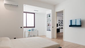 A bedroom with a bed, a desk with a laptop, a TV, and a bookshelf.