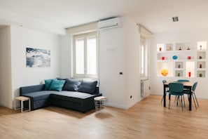 A modern living room with a sectional sofa, a dining table with chairs, and a built-in shelf unit with decorative items. - Casa di Vetro 1 Apartment by Wonderful Italy (Palermo)