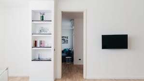 A modern living room with a flat-screen TV mounted on the wall, a bookshelf with various items, and a doorway leading to another room.