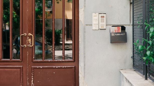 A brown door with a glass panel, a mailbox, and a small outdoor area with a concrete bench.