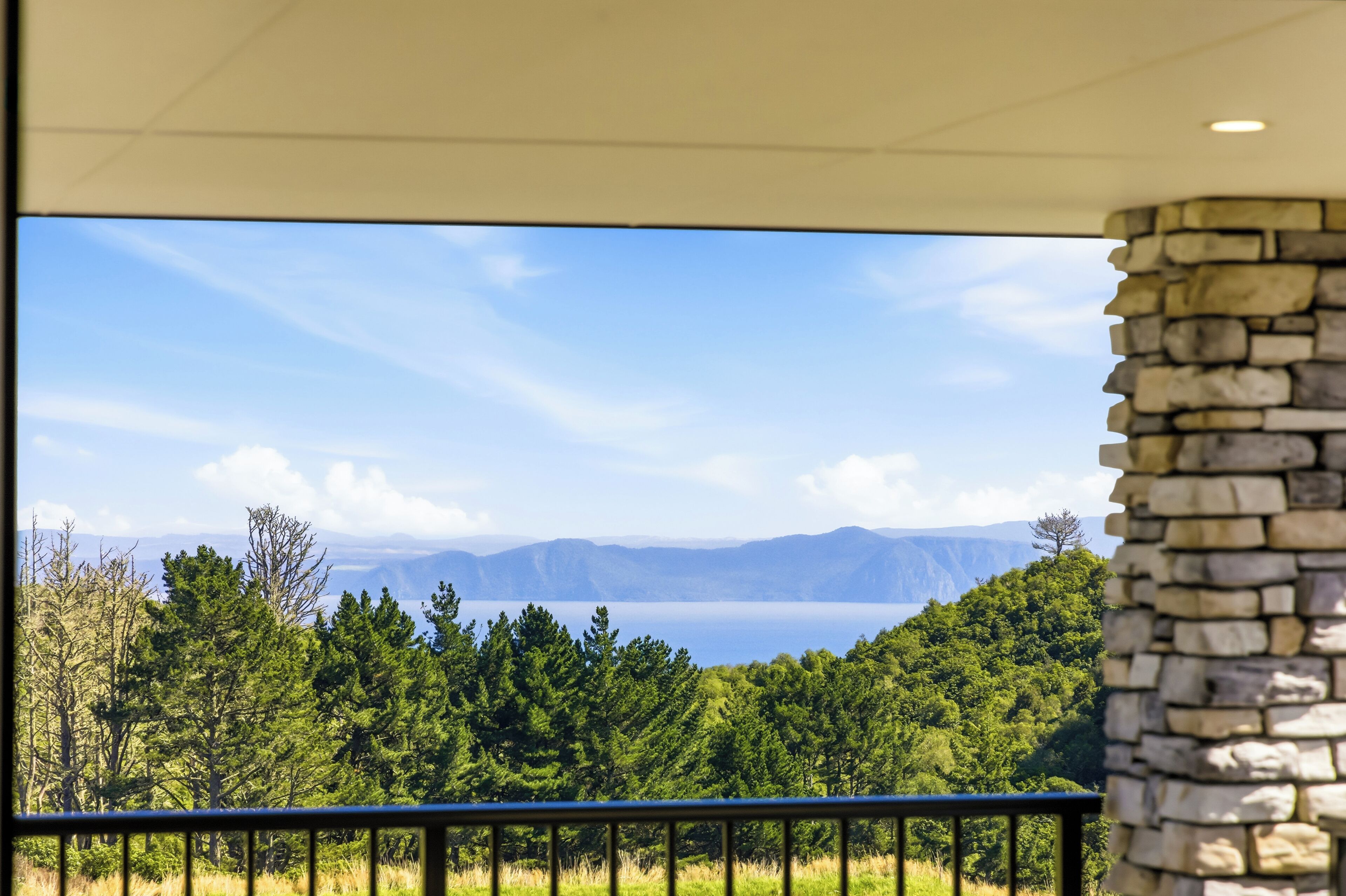 A view from a balcony with a stone wall, overlooking a lake and distant mountains.