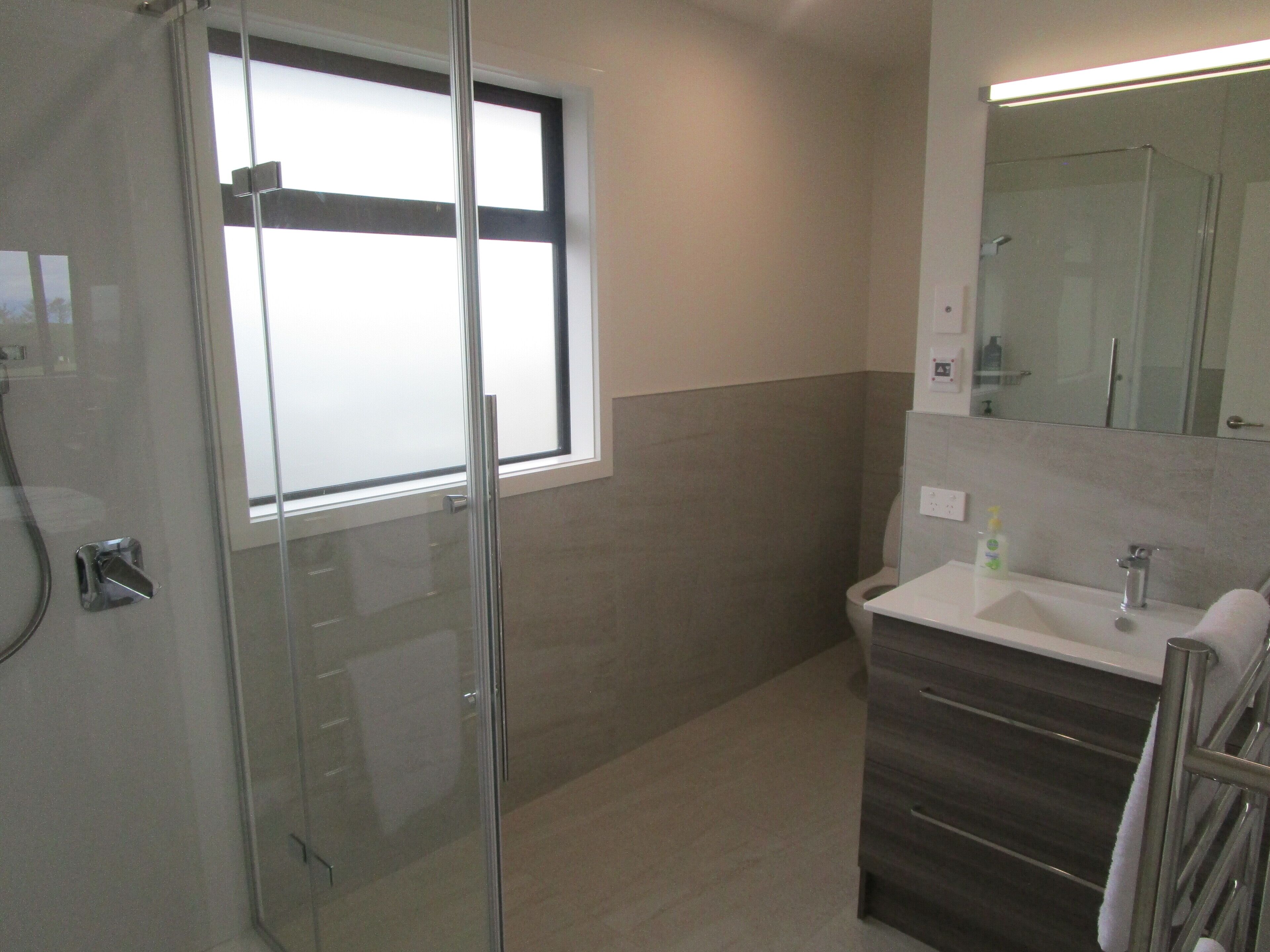A modern bathroom with a glass shower enclosure, a window, a sink with a mirror, and a towel rack.