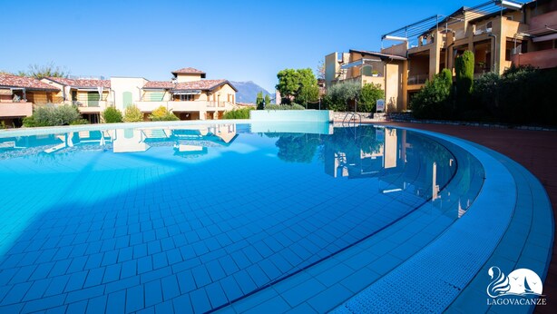 Une piscine dotée d’une terrasse carrel ée, entourée d’immeubles à plusieurs étages avec des balcons, sous un ciel dégagé.
