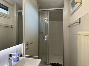 A bathroom with a glass-enclosed shower, a white sink with a soap dispenser, and a towel rack. - Gästehaus Elzblick (Rust)