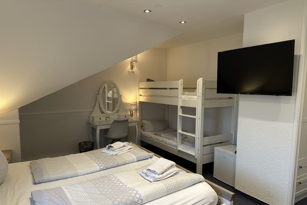 Una camera da letto con letti a castello, una scrivania con uno specchio, una televisione e un cestino dei rifiuti.