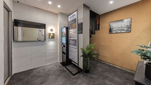 Un área de recepción con diseño moderno, que incluye un mostrador de recepción, un panel informativo digital, un espejo grande y un cuadro enmarcado en la pared.