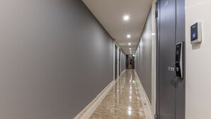 Un largo pasillo de hotel estrecho, con paredes grises, suelo de mármol y una serie de puertas a la derecha.