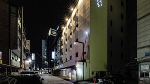 Vista nocturna de una calle con un edificio que tiene un letrero de neón y ventanas iluminadas.