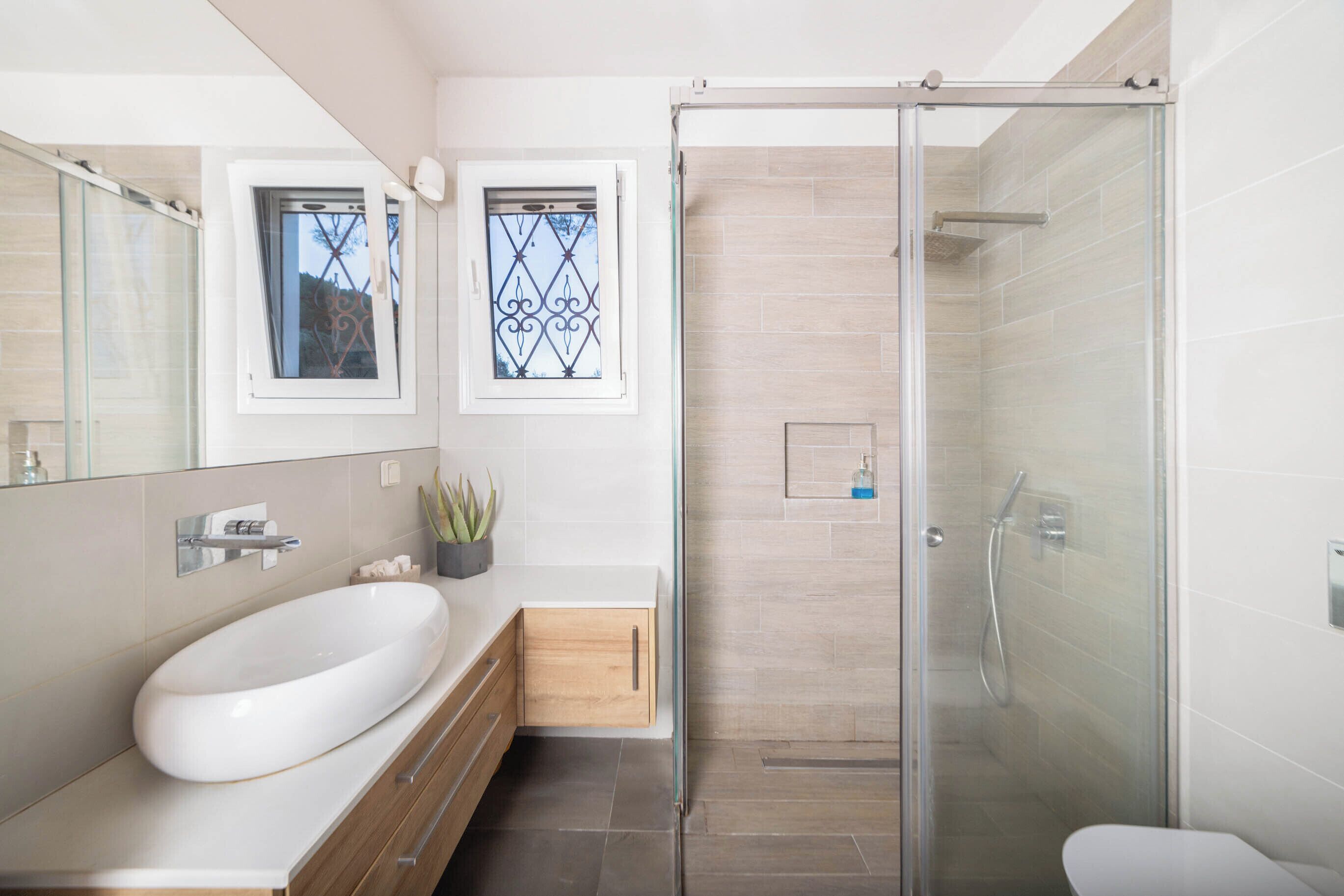 A modern bathroom with a large oval sink, a glass-enclosed shower, and a small window with decorative iron bars.