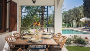 An outdoor dining area with a pool and greenery in the background.