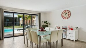 A modern dining area with a glass table and white chairs, a white cabinet with drawers, and a large wall clock.